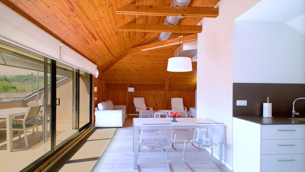 A modern interior with a wooden ceiling, a dining area with a table and chairs, a kitchen with a sink, and a view through large windows. - Casa de Vacaciones con pádel en Montseny by Can Forcadell (Breda)