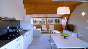 A modern kitchen with white cabinetry, a dining area with a table and chairs, and a television. - Casa de Vacaciones con pádel en Montseny by Can Forcadell (Breda)