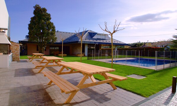 Un patio trasero con piscina, mesas de picnic y un patio de piedra.