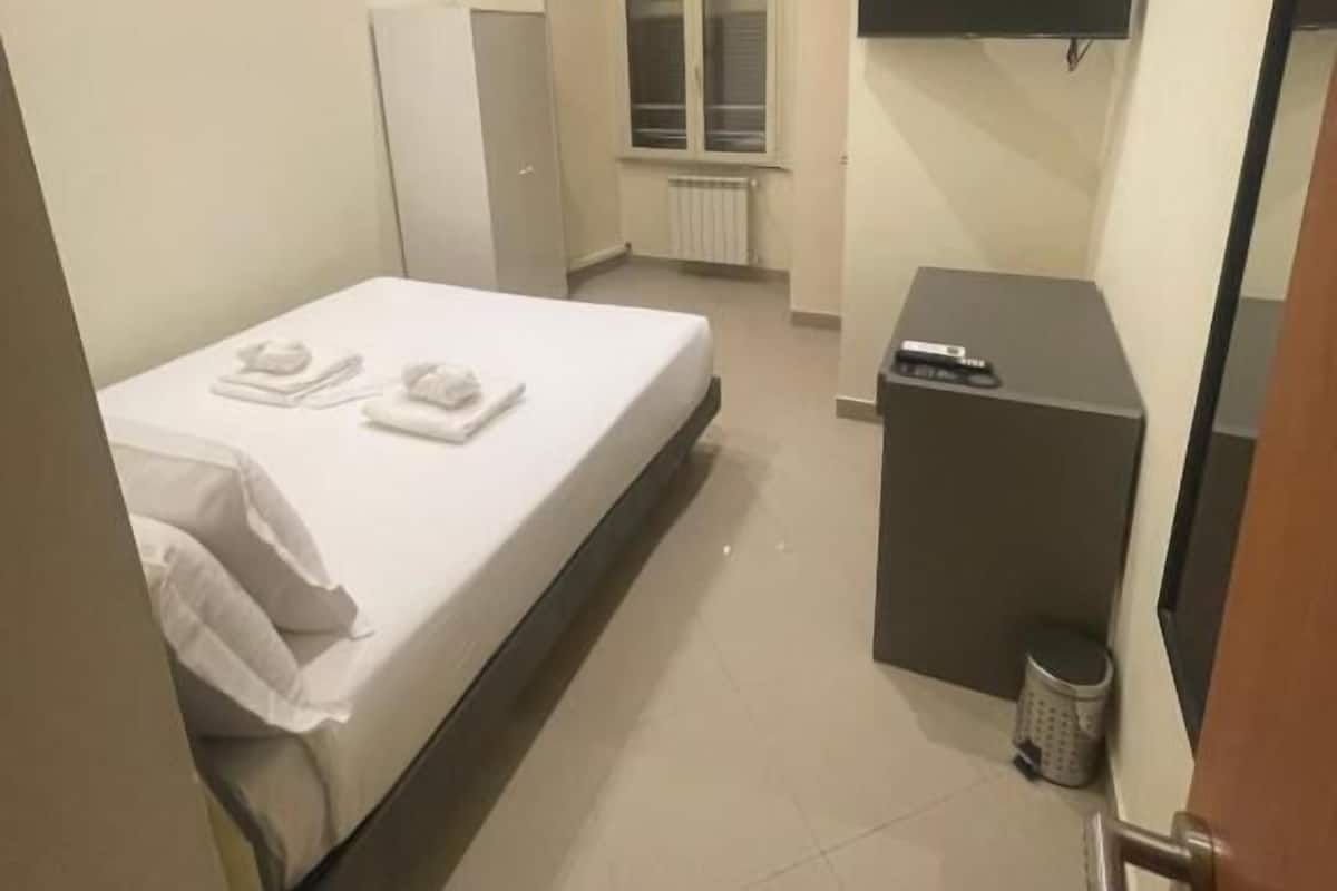 Una habitación de hotel con cama, televisión, escritorio, radiador y ventana.