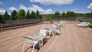 A wooden deck with outdoor seating, including tables and chairs, overlooking a forested area. - Charming Condo | Ski-in/Ski-out + Pool Access (Champion)