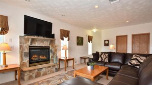 A living room with a stone fireplace, a flat-screen TV, a leather sofa, and a coffee table.