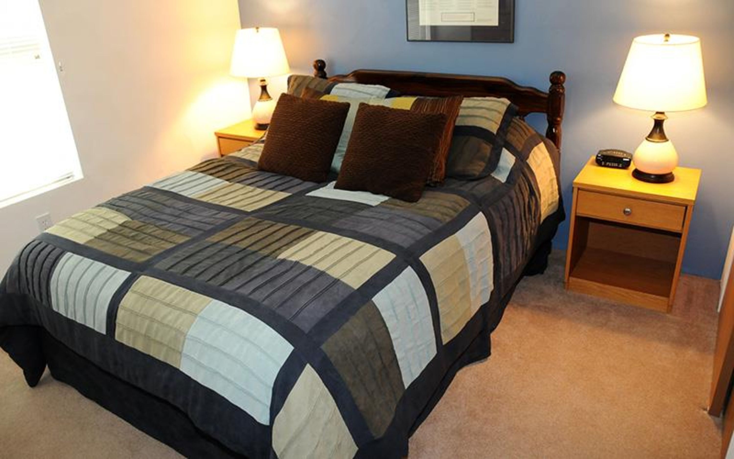 A neatly made bed with a quilt, two bedside tables with lamps, and a framed certificate on the wall.