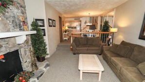 Ein gemütliches Wohnzimmer mit Kamin, einer Couch, einem Couchtisch und einer Treppe, die zur Küche führt.