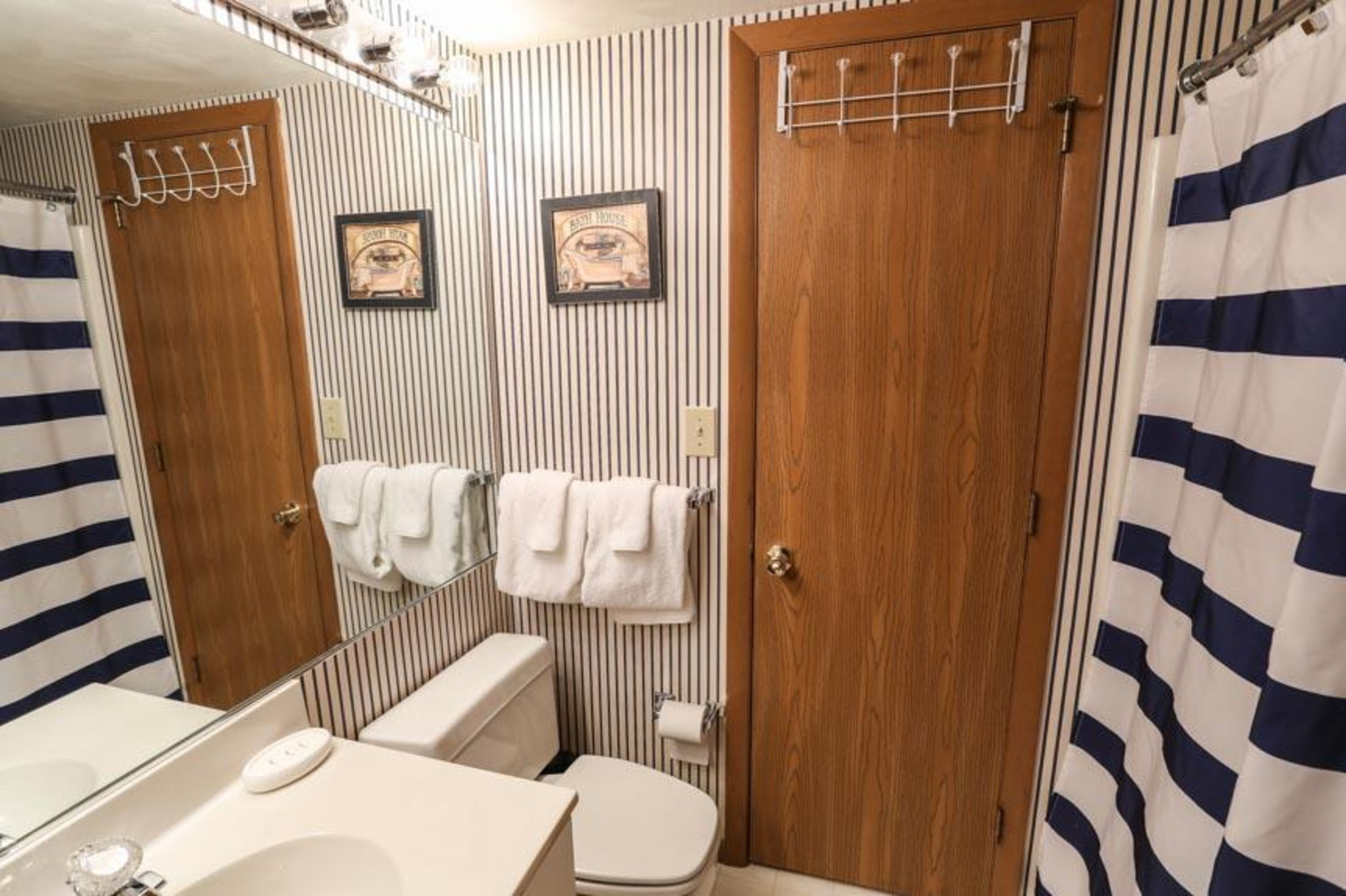 A bathroom with striped wallpaper, two wooden doors, a sink, and a toilet.