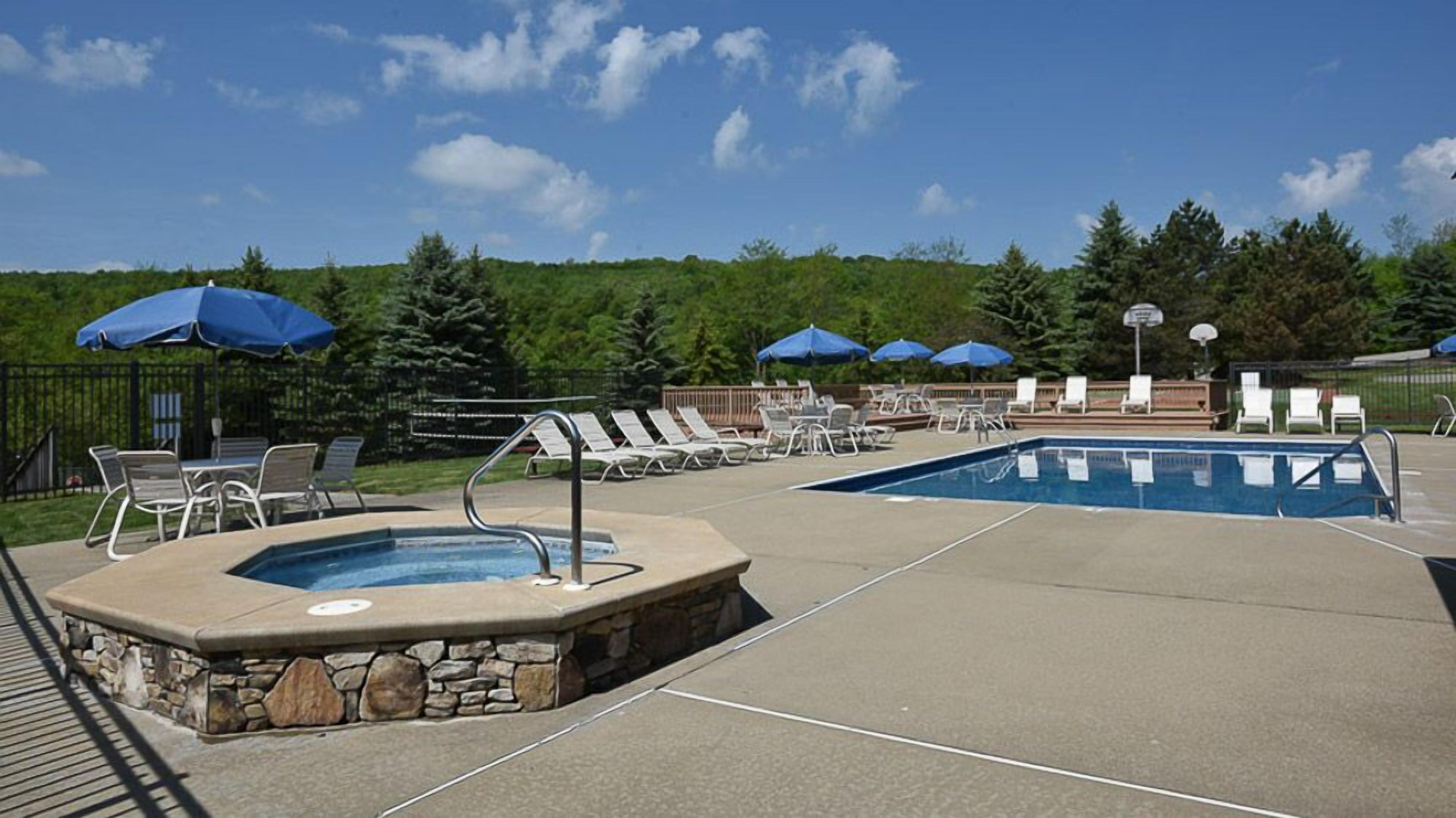A pool area with lounge chairs and umbrellas, surrounded by a stone wall and a basketball hoop.