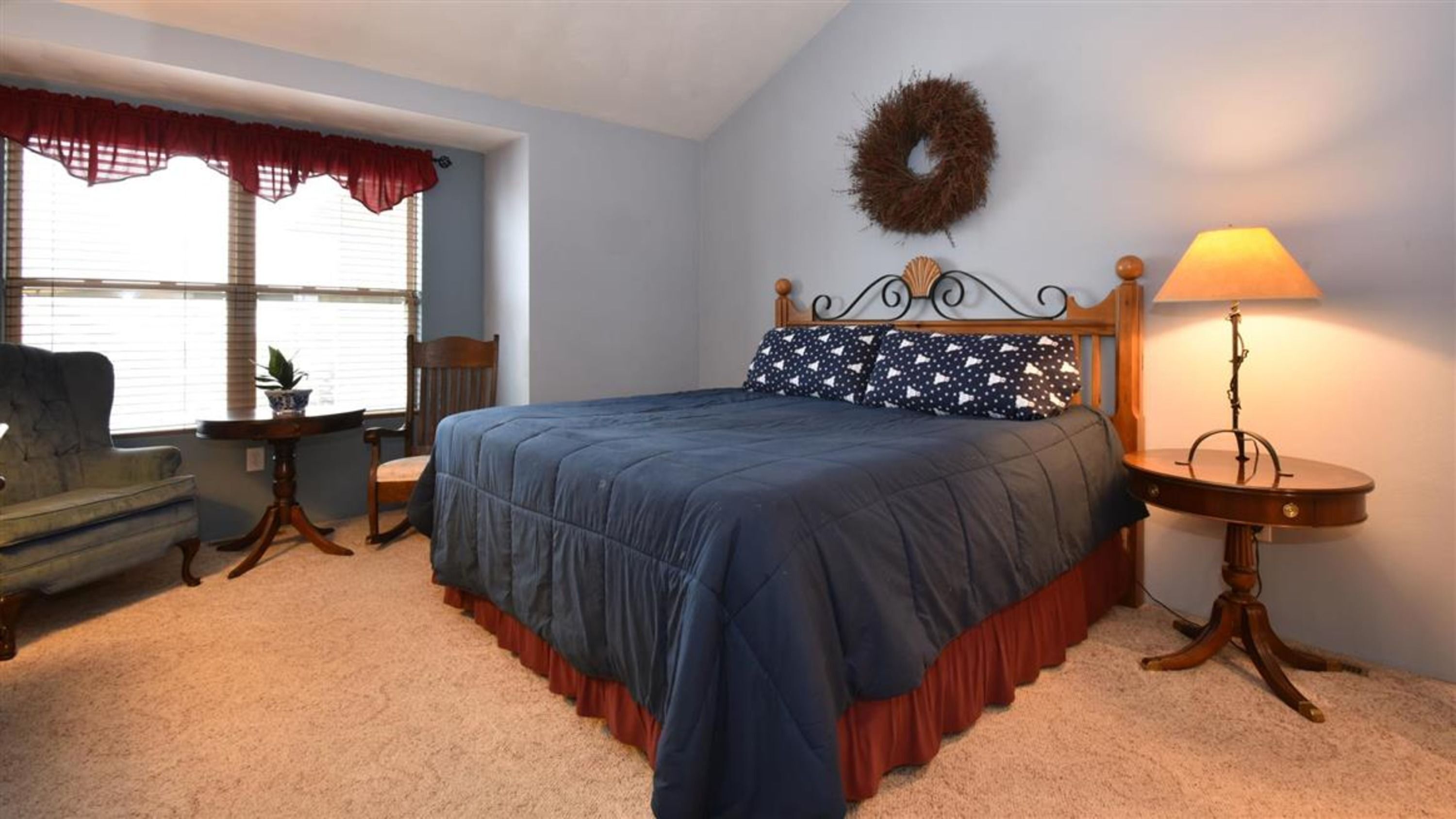 A bedroom with a bed, a chair, a lamp, a window with curtains, and a wall decoration.