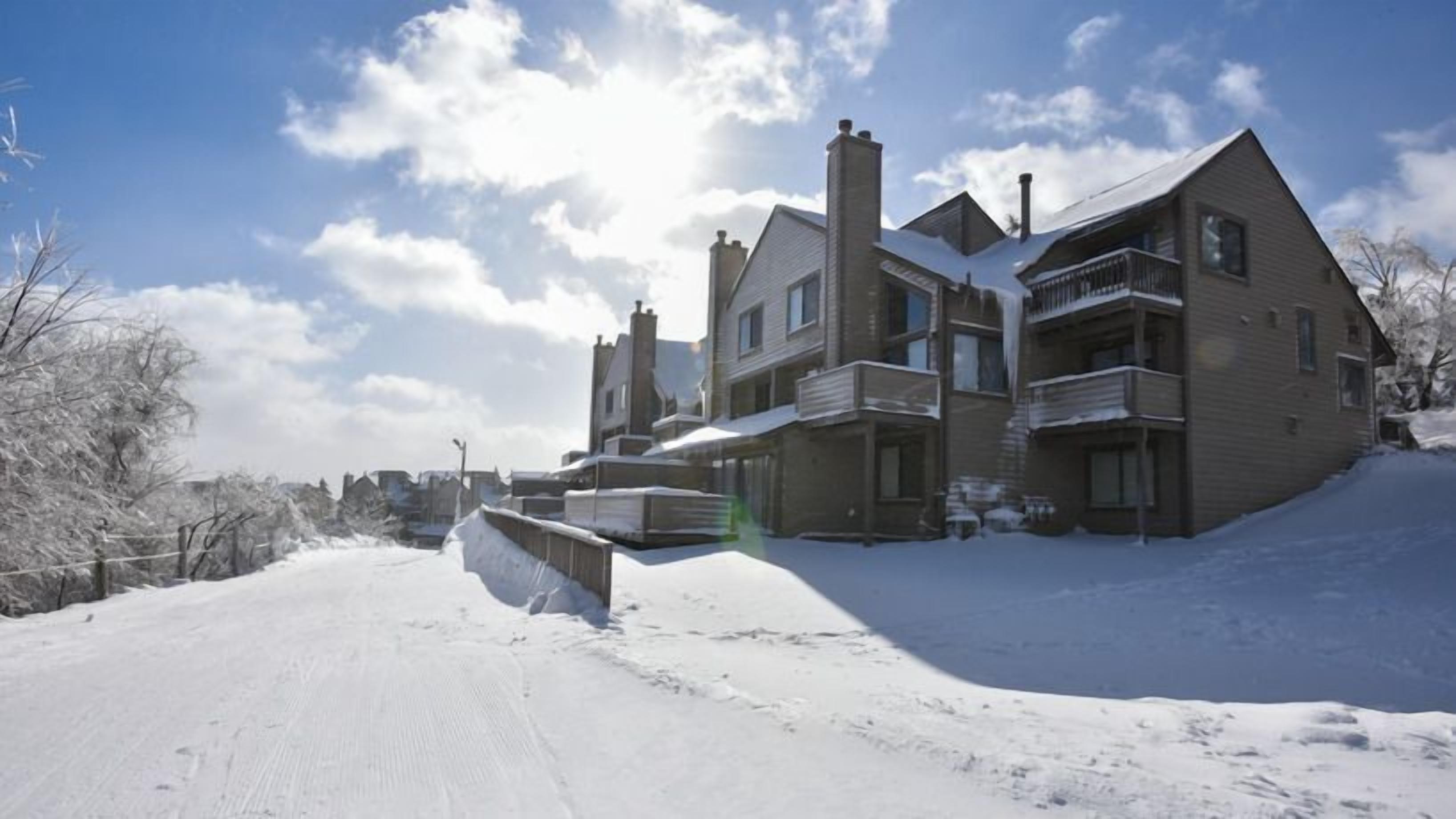 Nestled amidst a serene blanket of snow, the charming Villages Condos at Seven Springs Resort gleam under a bright winter sun, inviting guests to enjoy a cozy retreat in Champion, Pennsylvania.