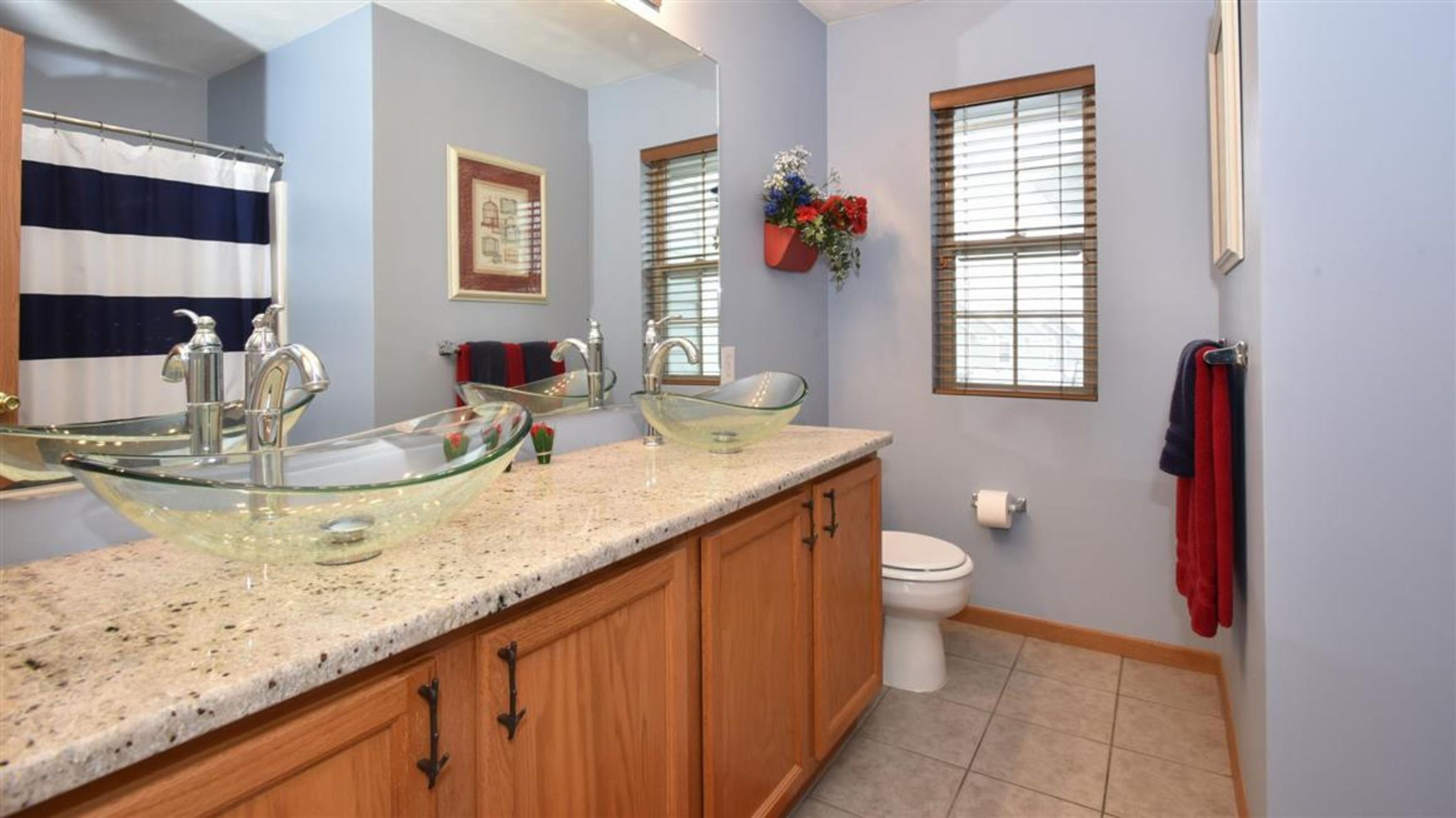 A bathroom with a glass vessel sink, wooden cabinets, a toilet, and a shower curtain.