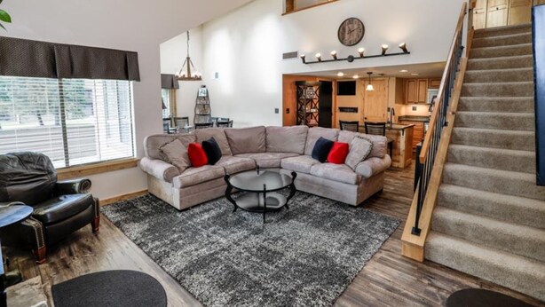 A spacious living area with a sectional sofa, a coffee table, and a staircase leading to an upper level. - Sleek 2BR Loft | Near Slopes + Shuttle & Pools (Champion)