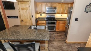 A kitchen with granite countertops, wooden cabinets, stainless steel appliances, and a bar stool. - Sleek 2BR Loft | Near Slopes + Shuttle & Pools (Champion)
