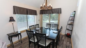 A dining area with a rectangular table set for six, surrounded by six chairs with cushioned seats. There is a chandelier above the table, and the room has wooden flooring. - Sleek 2BR Loft | Near Slopes + Shuttle & Pools (Champion)