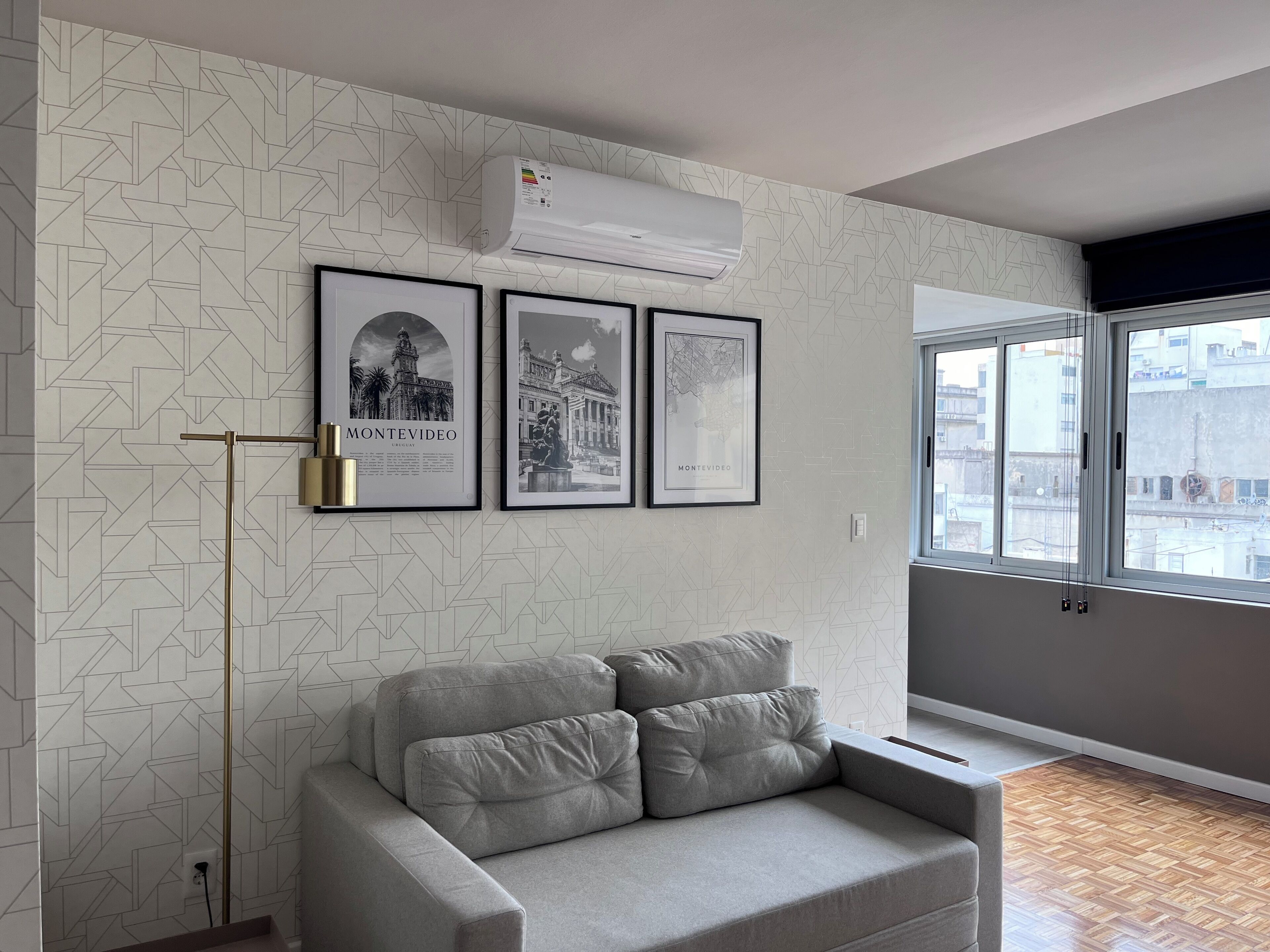 A modern living room with a grey sofa, a floor lamp, and framed pictures on the wall.