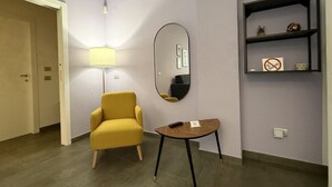 Una habitación con un sillón amarillo, una pequeña mesa redonda, un espejo y una estantería con un cartel de 'no fumar'.