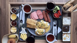 Un plateau contenant divers éléments pour le petit-déjeuner, notamment des œufs, des saucisses, du jambon et des toasts, ainsi que des condiments et des boissons.