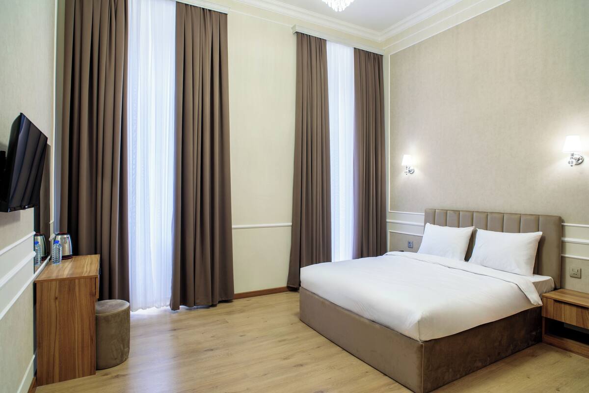 Camera d'albergo con un letto grande, comodini in legno, una TV e un piccolo angolo salotto.