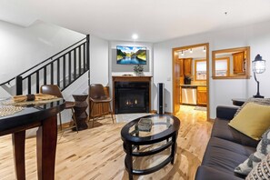 A modern living room with a fireplace, a dining area with a round table, and a staircase leading to another level. - Peaceful Downtown Gem with Fireplace & Patio (Coeur d'Alene)