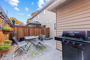A backyard with a barbecue grill, a table, and two chairs. - Peaceful Downtown Gem with Fireplace & Patio (Coeur d'Alene)