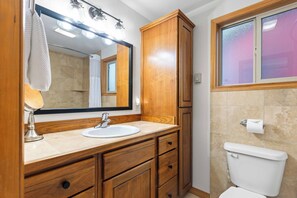 A bathroom with a wooden vanity, a sink, a mirror, a toilet, and a window with frosted glass. - Peaceful Downtown Gem with Fireplace & Patio (Coeur d'Alene)