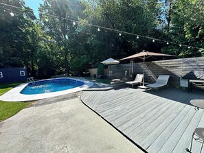 Un pati amb piscina, terrassa de fusta, gandules i llums penjants.