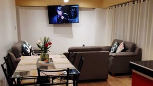 A modern living room with a dining area, a flat-screen TV mounted on the wall, a sofa, and a red cabinet. - Rosaelena b&b tours and experiences with transportation included 7persons (Cusco)