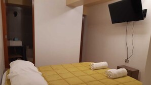 A hotel room with a bed, two rolled towels, a TV mounted on the wall, and a small wooden nightstand. - Rosaelena b&b tours and experiences with transportation included 7persons (Cusco)