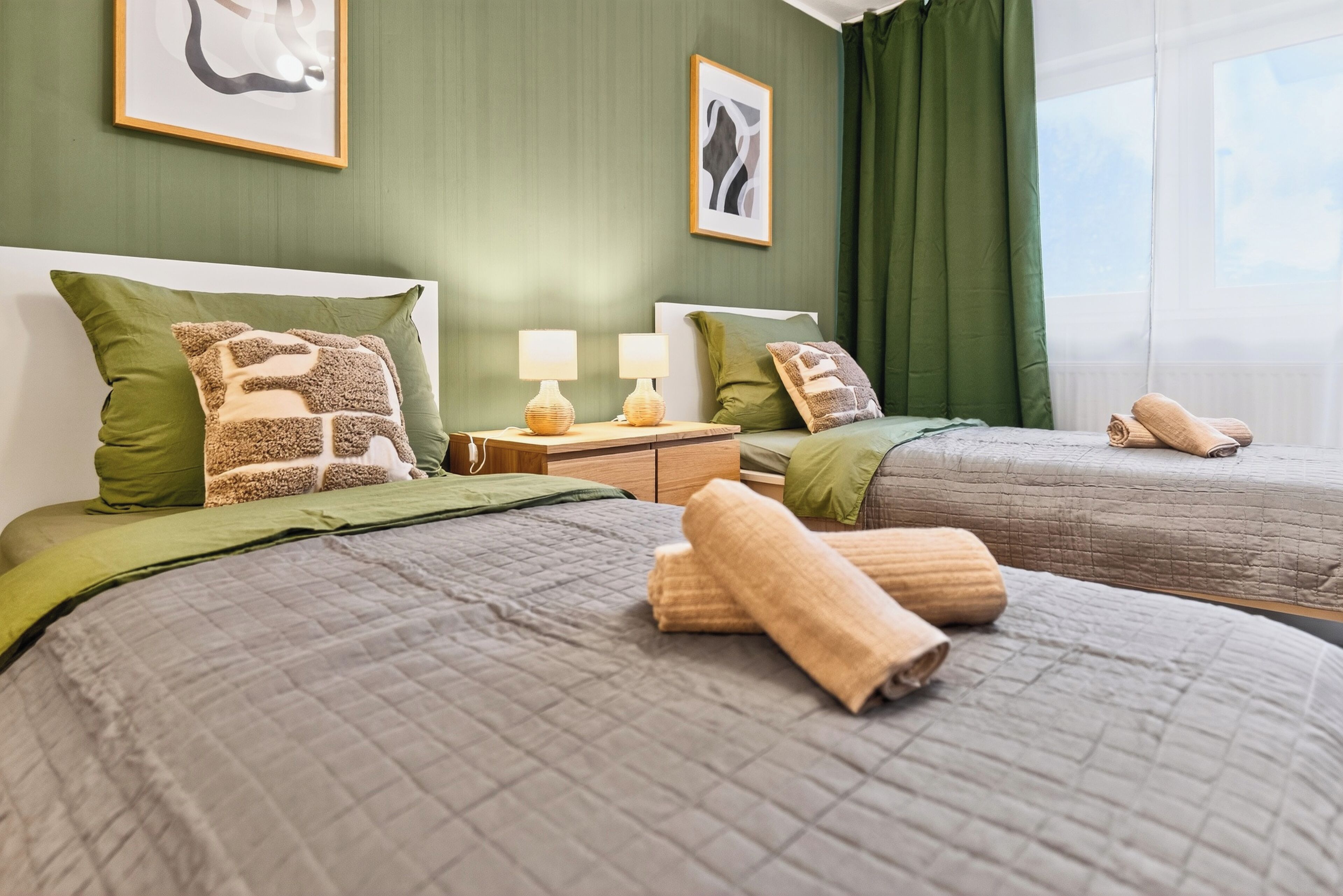 A hotel room with two beds, green walls, and artwork.