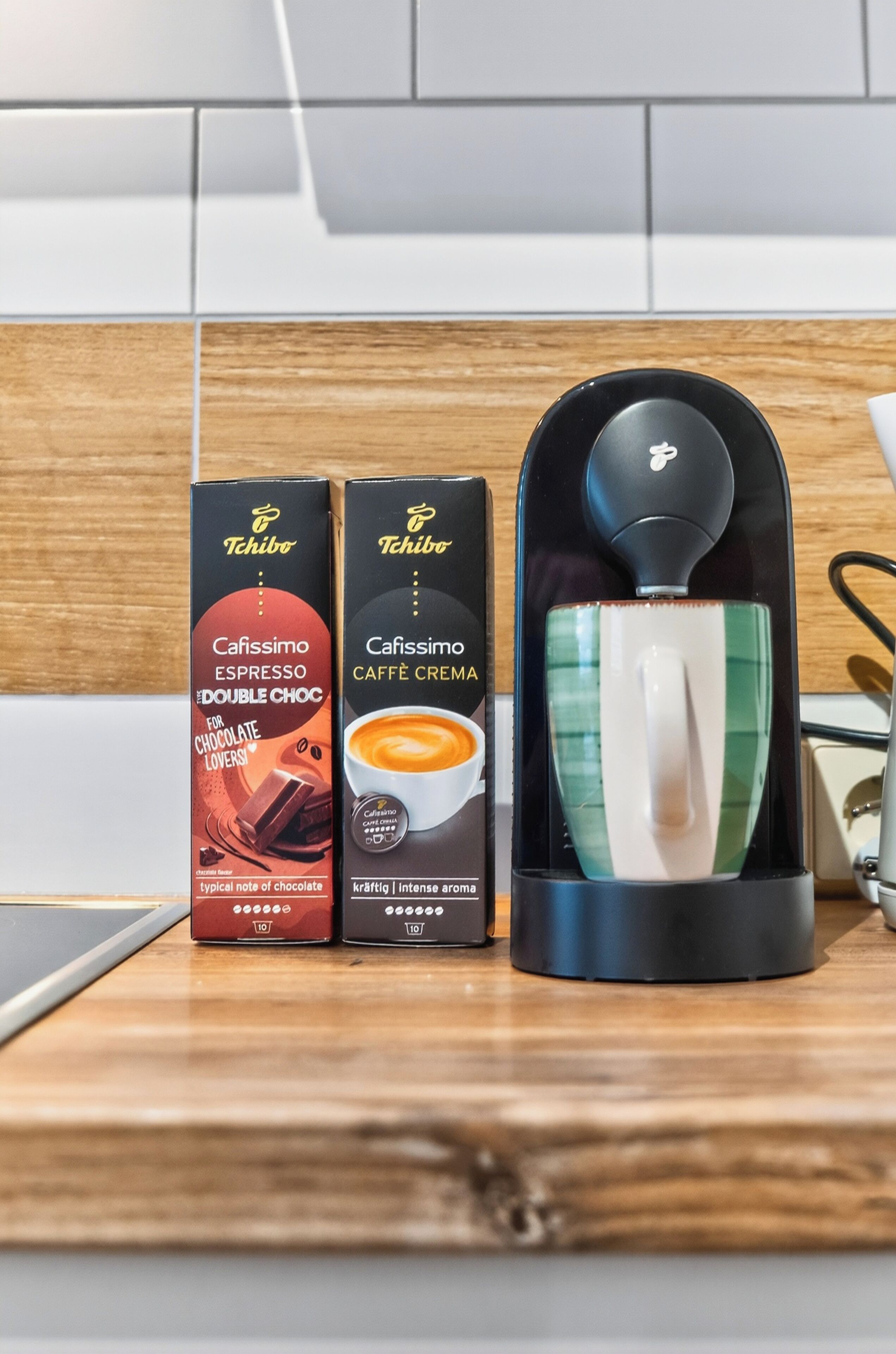 Due confezioni di caffè Tchibo e una macchina da caffè su un tavolo di legno.