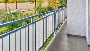 A covered balcony with a view of a parking lot and trees. - Tina in Buchen (Buchen)