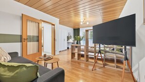 A modern living room with a wooden ceiling, a sofa, a coffee table, and a TV on a stand. - Tina in Buchen (Buchen)
