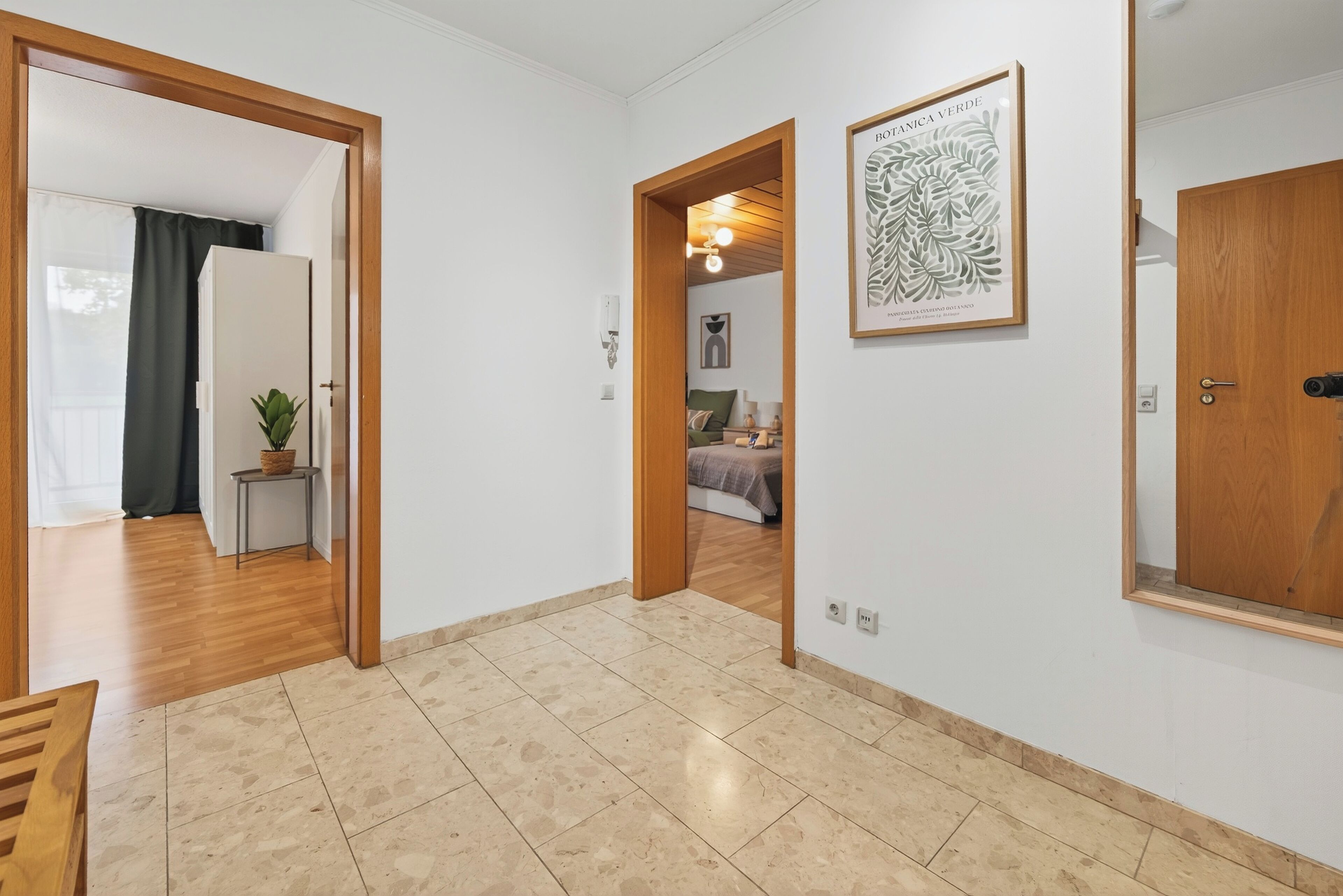 A hallway with a wooden floor, a door on the right, and a framed botanical print on the wall.