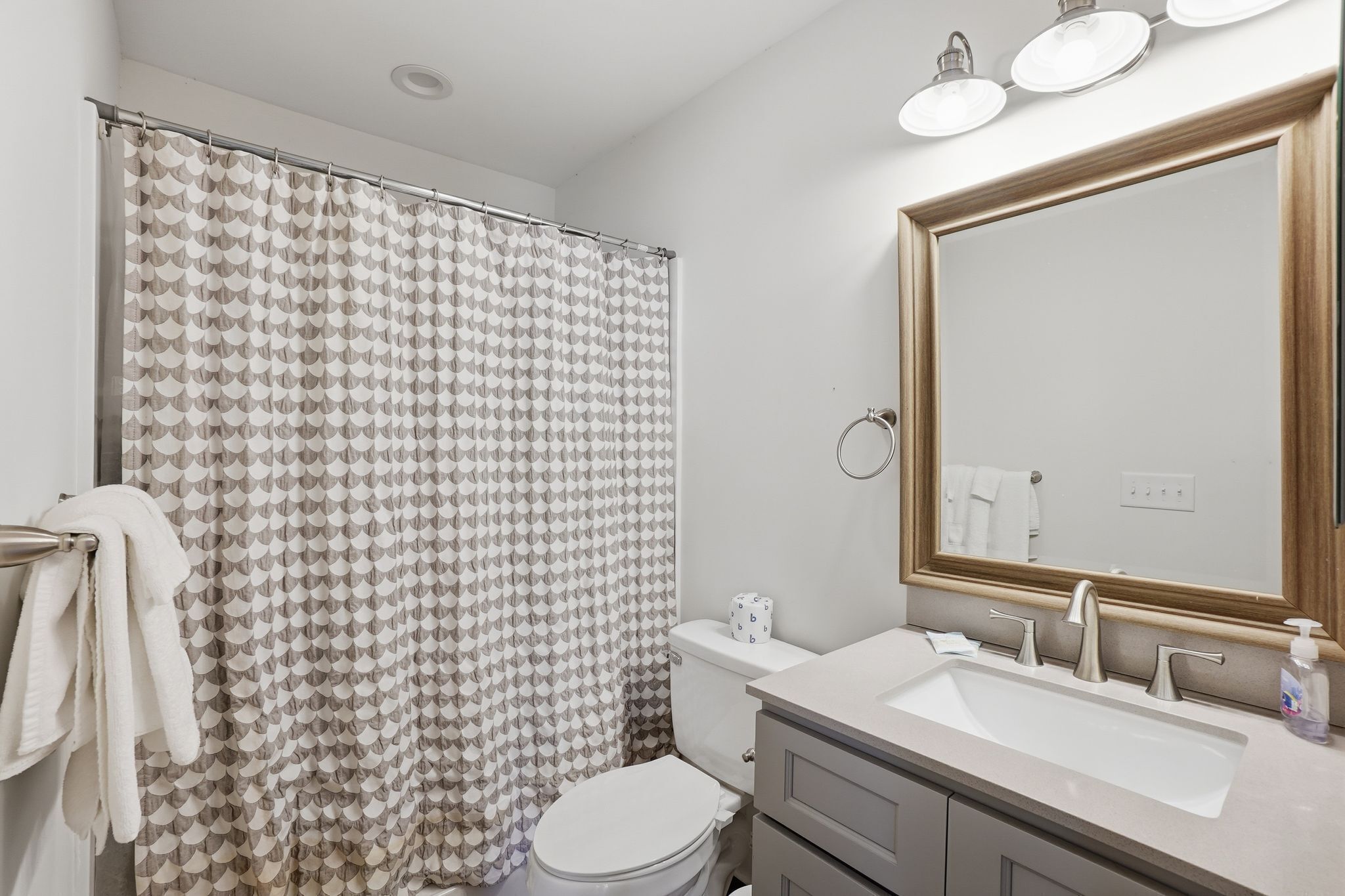 Une salle de bain équipée d’un rideau de douche, de toilettes, d’un lavabo, d’un miroir et d’un porte-serviettes.