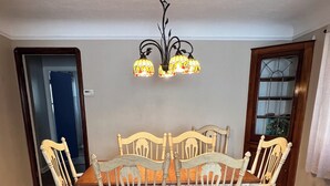 Een eethoek met een houten tafel en stoelen, een kroonluchter en een deur met raam.