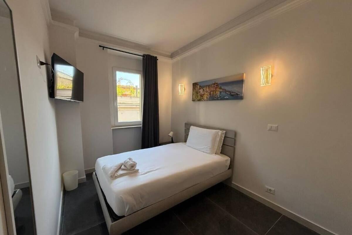 Habitación de hotel con cama, televisor de pantalla plana en la pared, ventana con cortinas y un cuadro colgado.