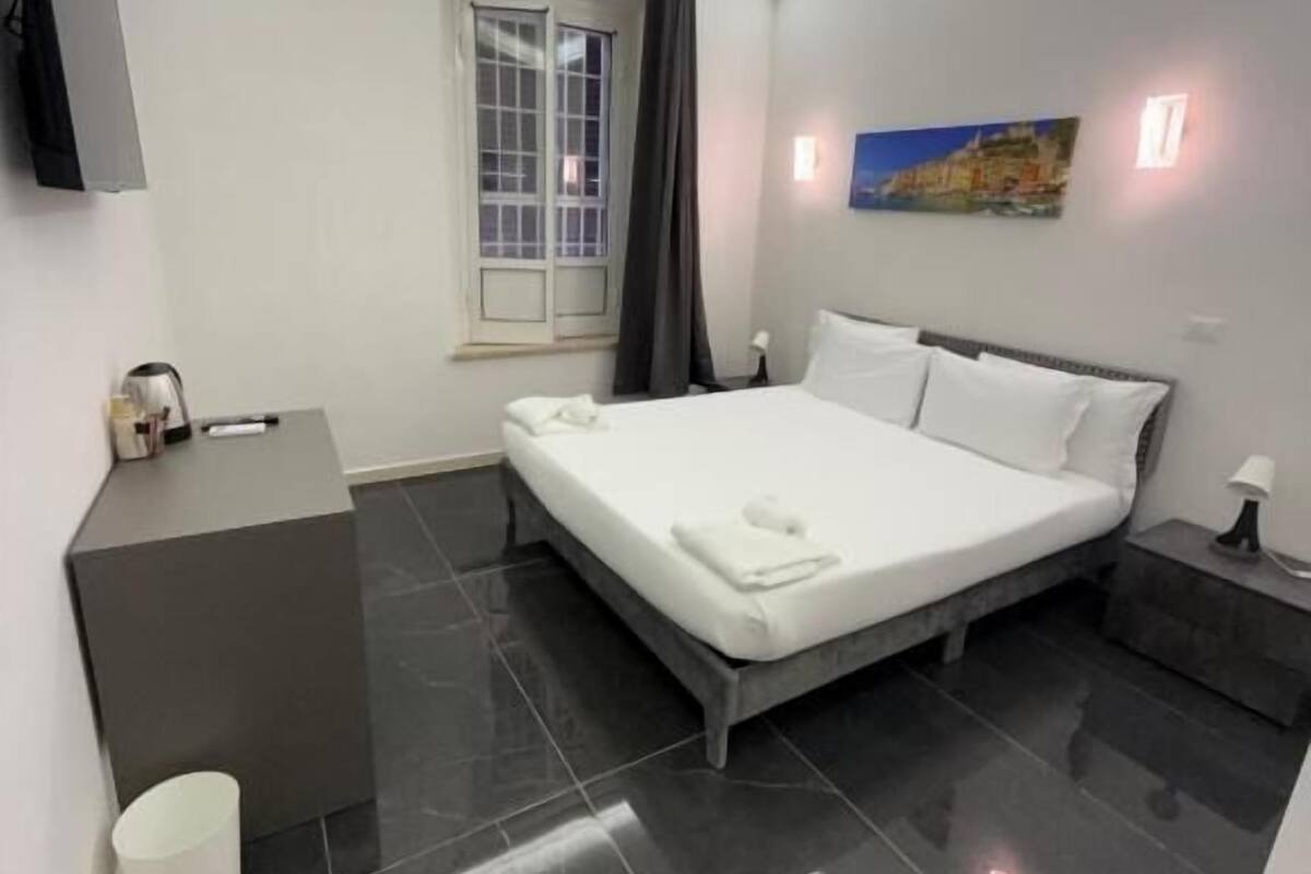 Un dormitorio moderno con cama, mesita de noche, escritorio y ventana con cortinas.