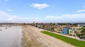 A coastal town with a sandy beach, boats, and colorful houses along the shore. - Mission Bay Waterfront | Patio Steps to the Sand (San Diego)