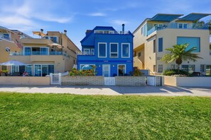 A modern residential building with a blue facade, numbered units, and a well-maintained lawn in the foreground. - Mission Bay Waterfront | Patio Steps to the Sand (San Diego)