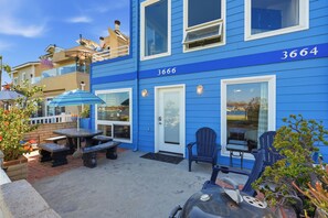 Un bâtiment bleu portant le numéro 3666, avec une terrasse aménagée de tables et de chaises, et un barbecue.
