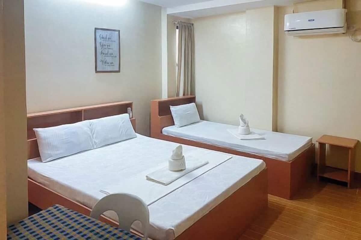 A hotel room with two beds, a small table, a chair, an air conditioning unit, and a curtain.