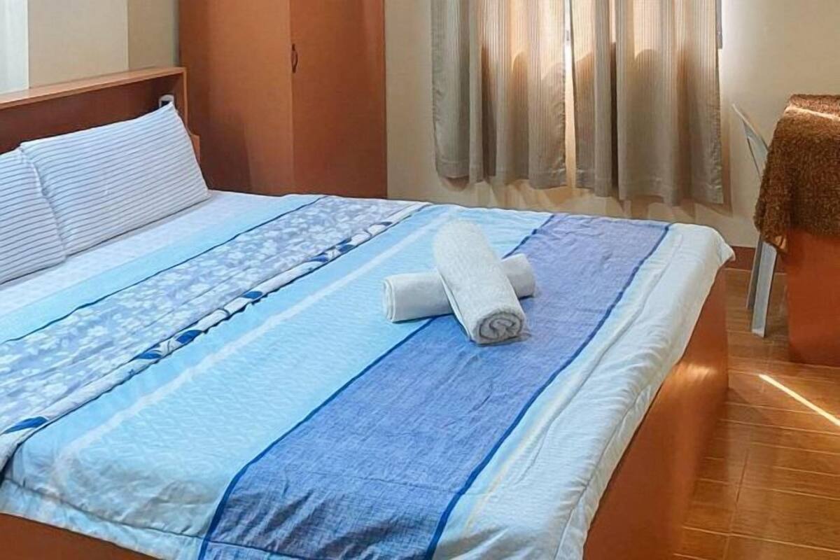 A neatly made bed with a striped bedspread, a rolled towel, and a wooden headboard.