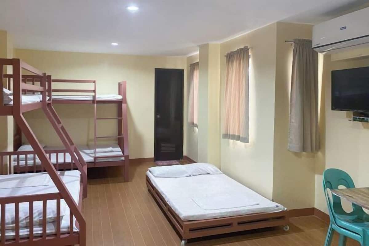 A dormitory room with bunk beds, a single bed, a desk, and an air conditioning unit.
