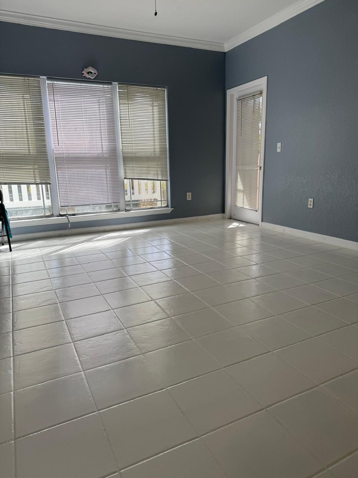 A spacious room with large windows, a door, and a tiled floor.