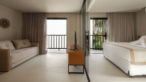 A modern hotel room with a sofa, a bed, a TV, and a balcony with a view. - Jubarte Flats  (Itacaré)
