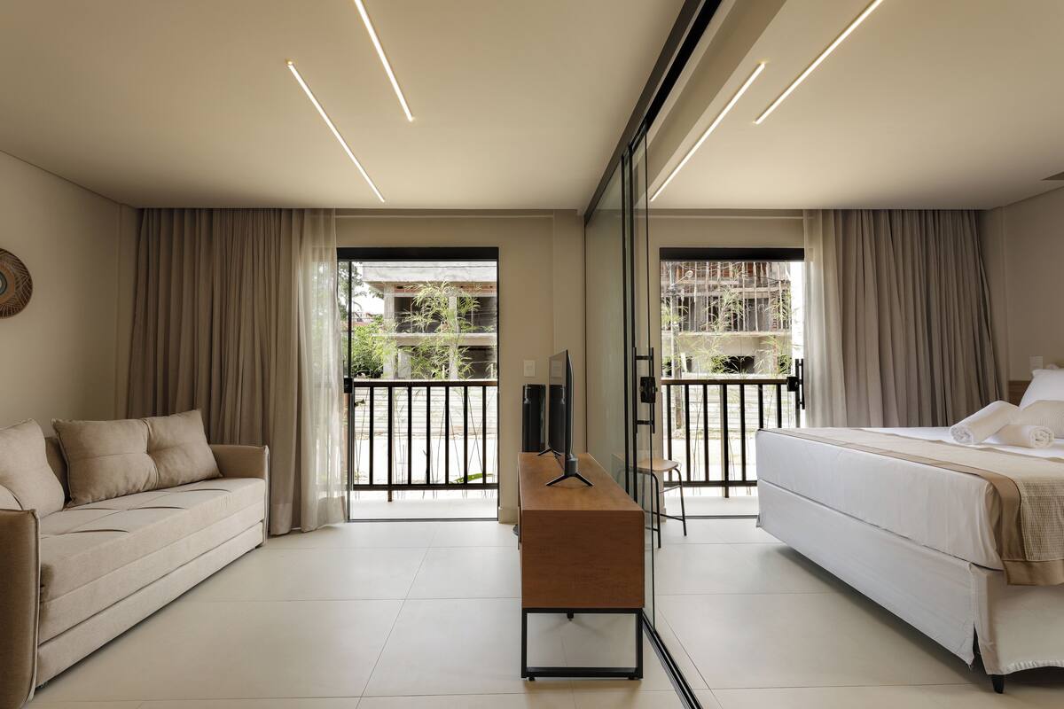 A modern hotel room with a sofa, a bed, a desk, and a large window.