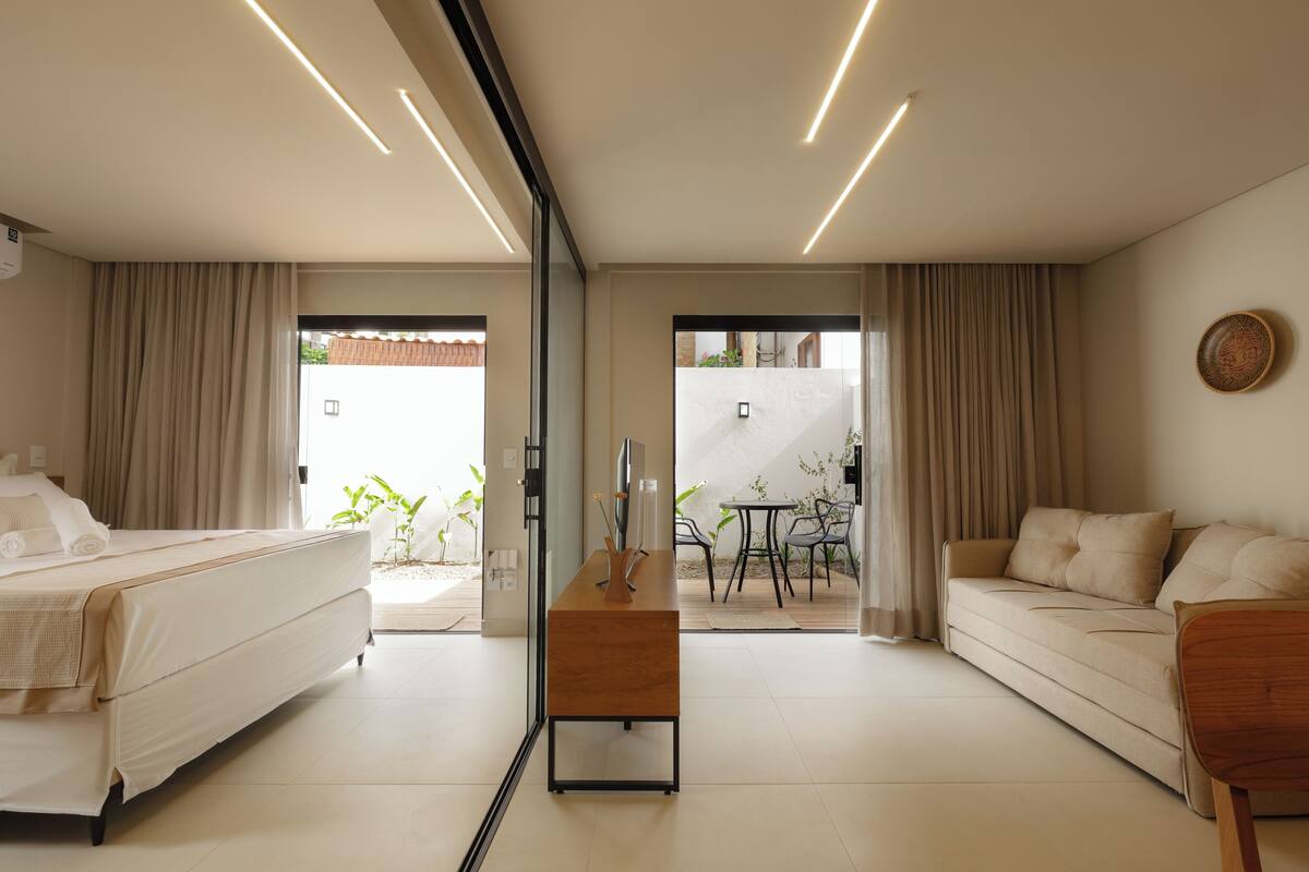 A modern hotel room with a bed, sofa, and a small table with a vase.