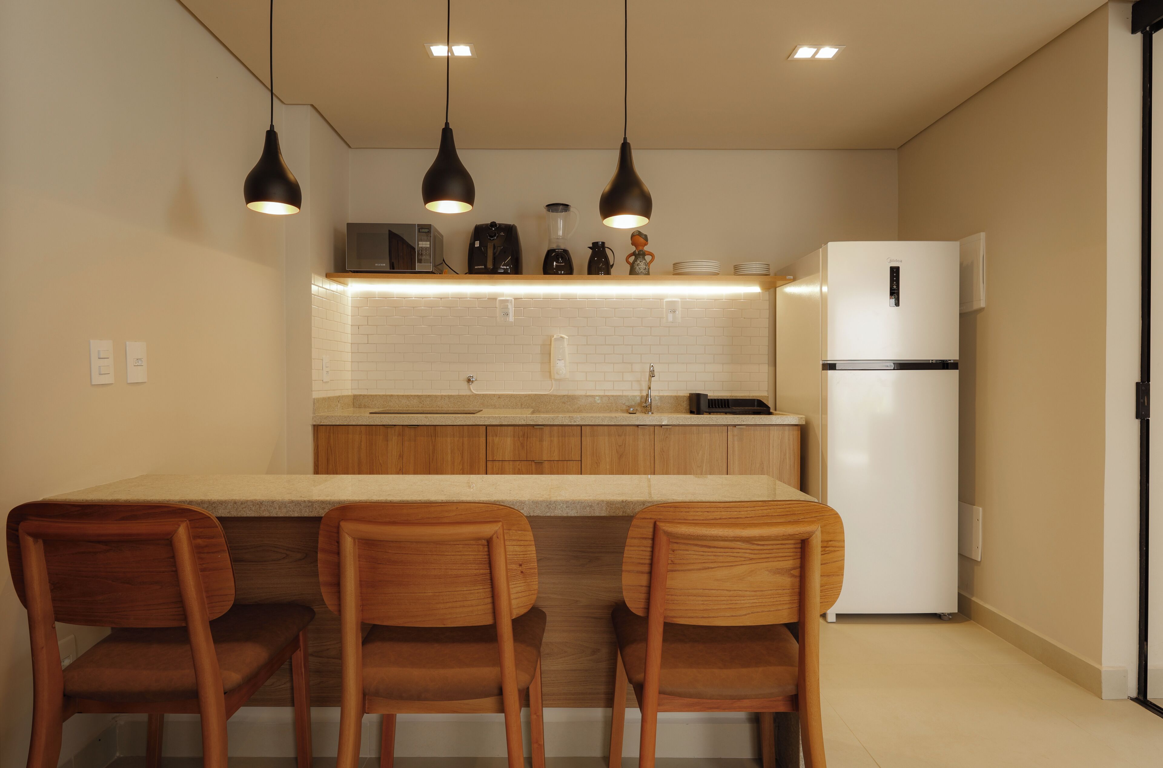 Una cuina moderna amb armaris de fusta, un refrigerador blanc i il·luminació penjant.