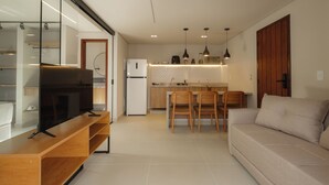 A modern kitchen with a dining area, a sofa, and a TV on a wooden stand. - Jubarte Flats  (Itacaré)