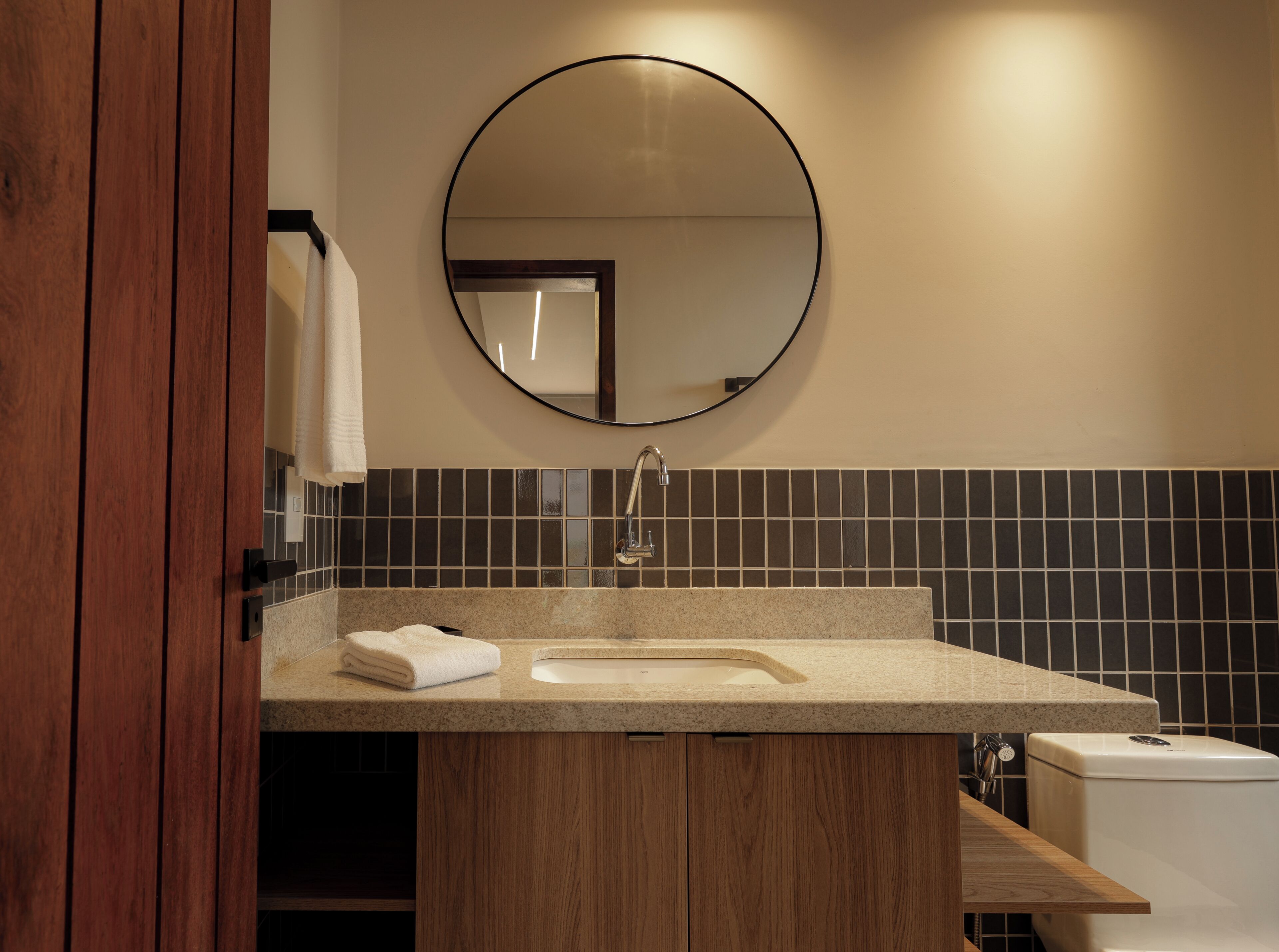 Un baño con tocador de madera, un espejo redondo y un salpicadero de azulejos.