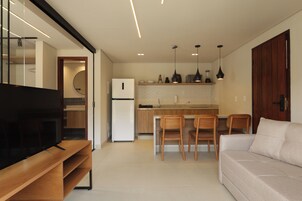Una cocina moderna con horno empotrado, un comedor con sillas de madera, un televisor sobre un mueble de madera y un sofá.