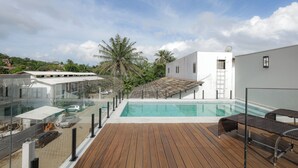A rooftop pool with a wooden deck, glass balustrade, and a view of surrounding buildings and palm trees. - Jubarte Flats  (Itacaré)